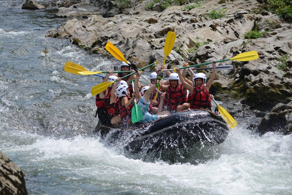 Eine Rafting-Gruppe hält ihre Paddel feierlich in die Höhe.