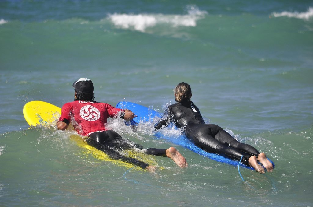 A participant in a surfing course in Spain is helped by the instructor while they are in the ocean.
