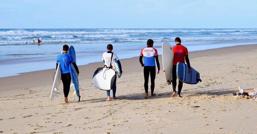 4 beginner surfers walk towards the sea.