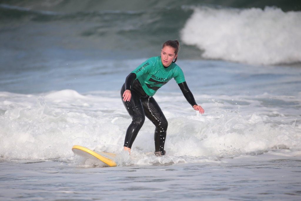 A beginner surfer standing on her surfboard riding a shallow wave.