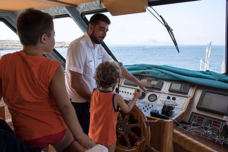 Durante una gita in barca alle isole Egadi il capitano mostra la cabina di comando a 2 bambini. 