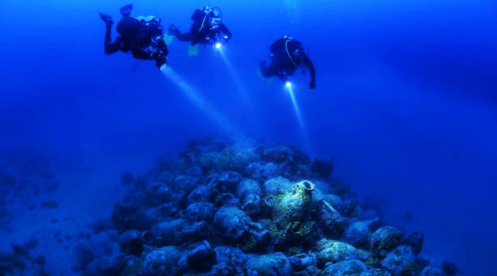 Tre sommozzatori ammirano le anfore di un'antica nave affondata nel mare Adriatico nella regione di Zara.