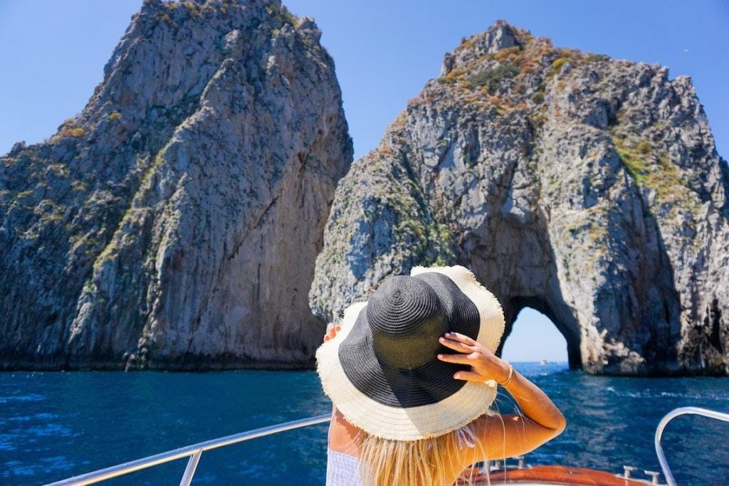 Eine Frau bewundert von ihrer Bootstour in Sorrent aus die Faraglioni.