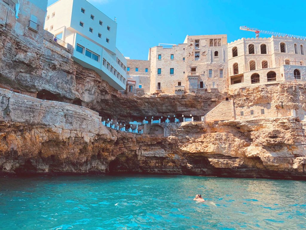 A man snorkeling in Polignano a Mare, beyond him you can see caves and houses. 