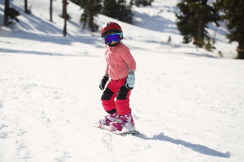 A little girl is learning how to snowboard.