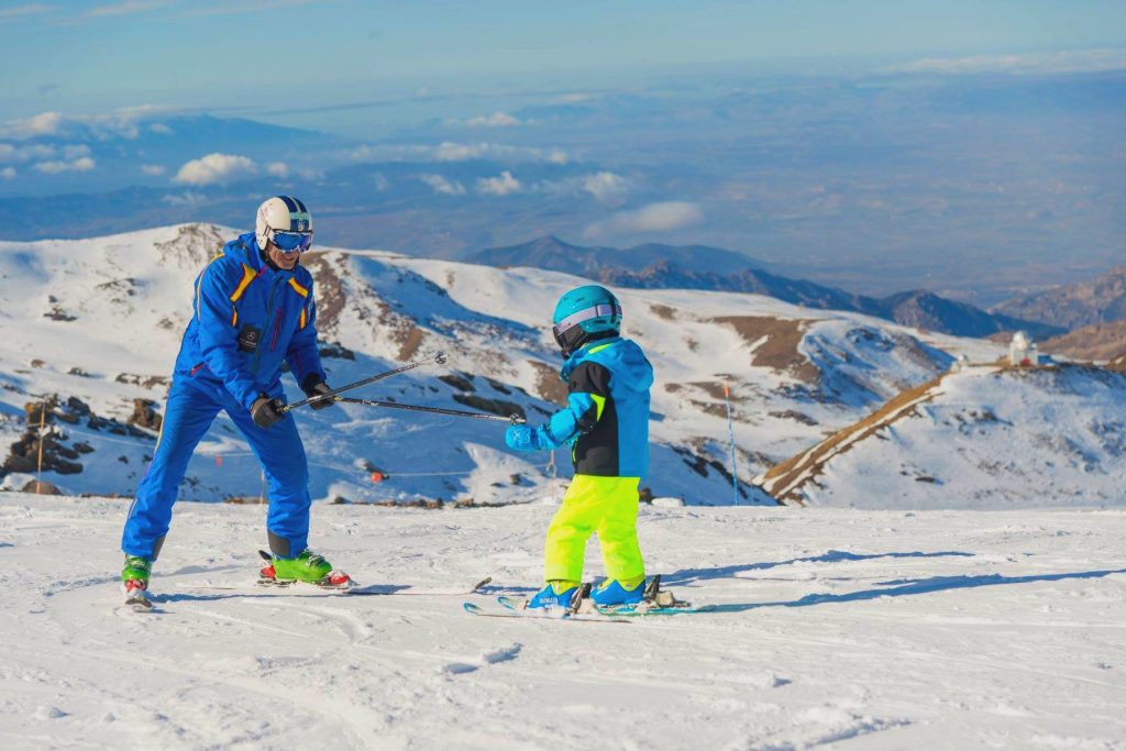 A kid takes a private ski lesson together with a ski instructor in Pradollano ski resort in Sierra Nevada. 