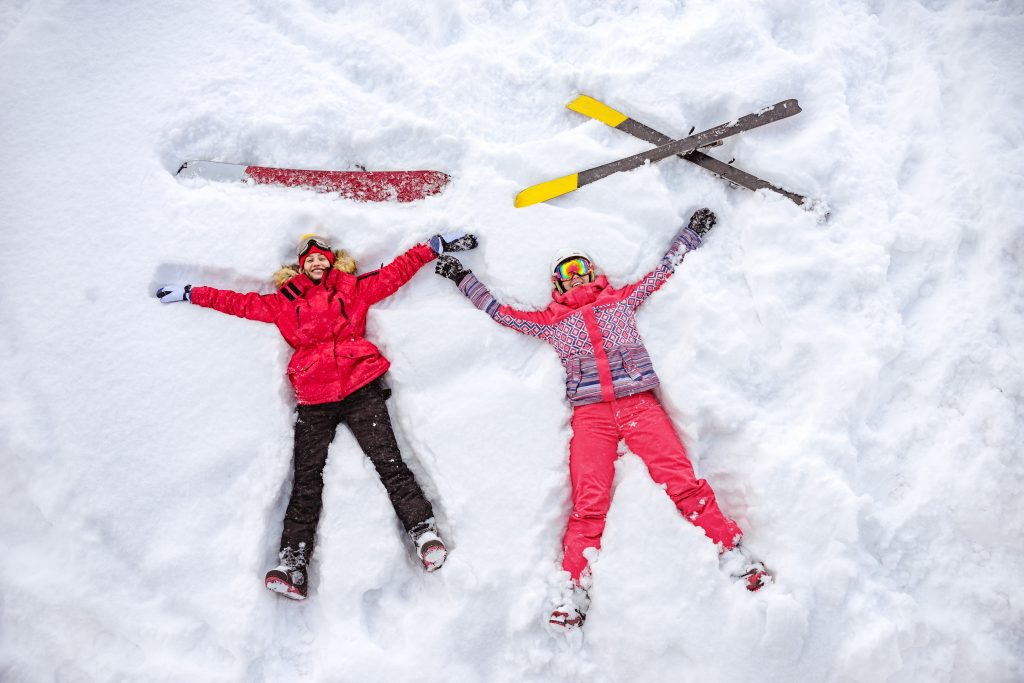 Two girls enjoy a day out in the snow with their ski and snowboarding equipment. 