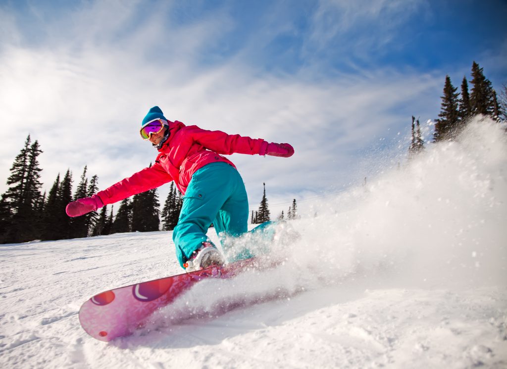 Eine Frau flitzt beim Snowboarden die Piste hinunter.