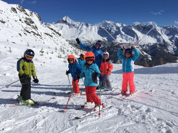  Kids standing on the snow with ski instructor and mountains in the background.
