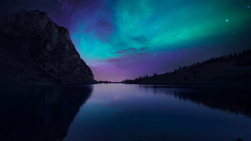A stunning view of the aurora borealis illuminating a serene mountain lake under a starry night sky.