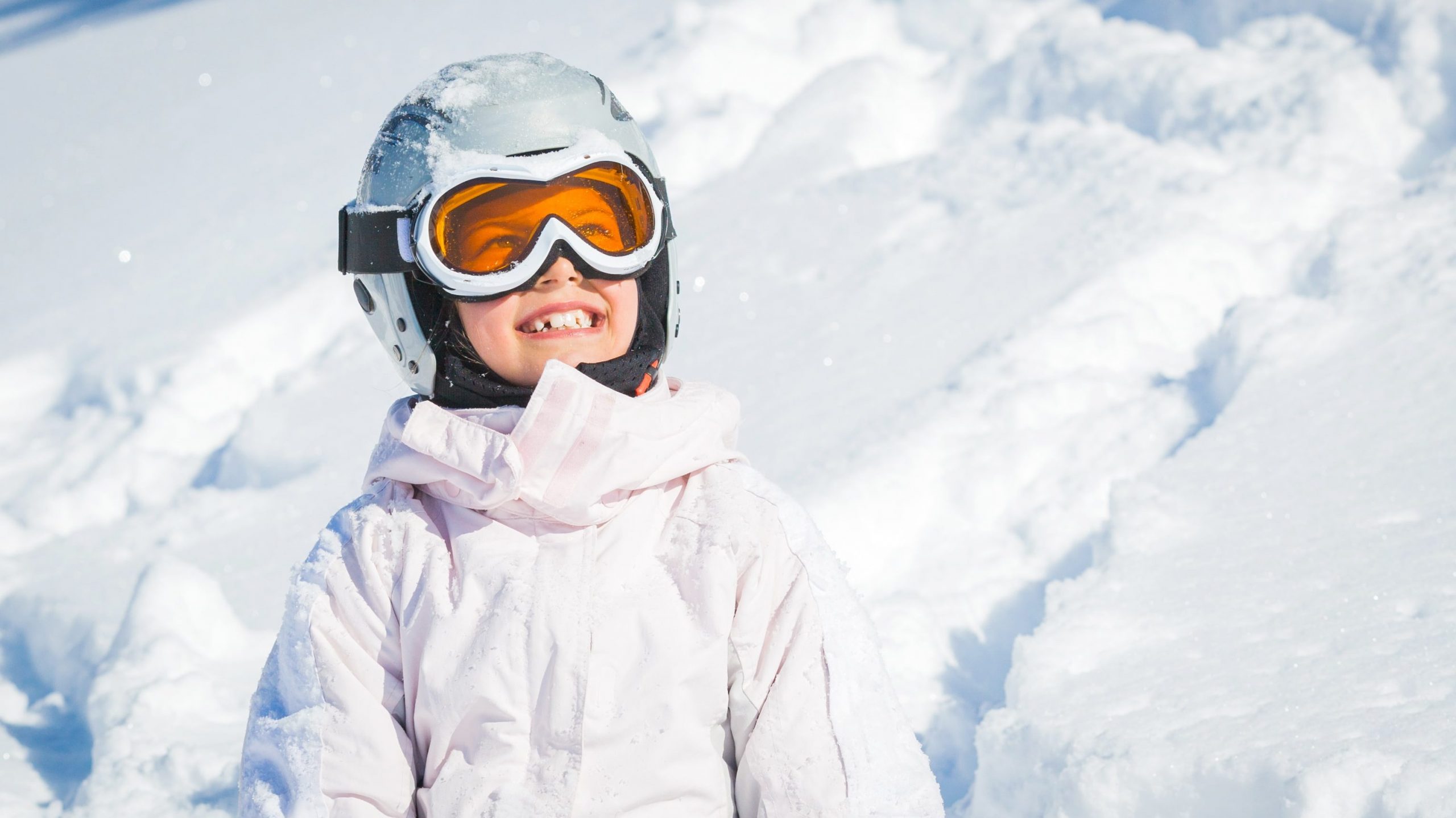 Ein Kind mit Skihelm und Skibrille lächelt in die Kamera