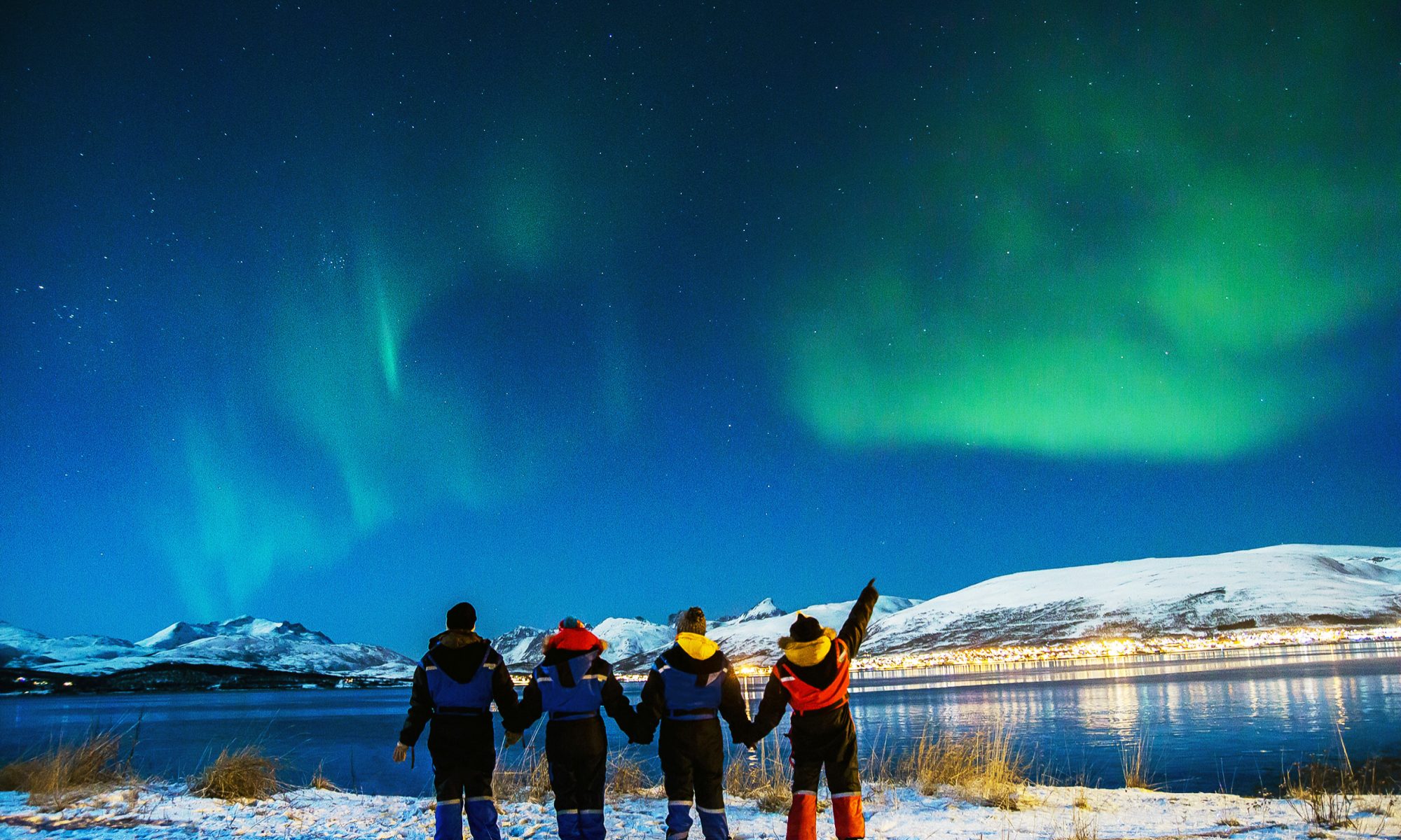 A group of friends admiring the Northern Lights illuminating the sky with mesmerising colours