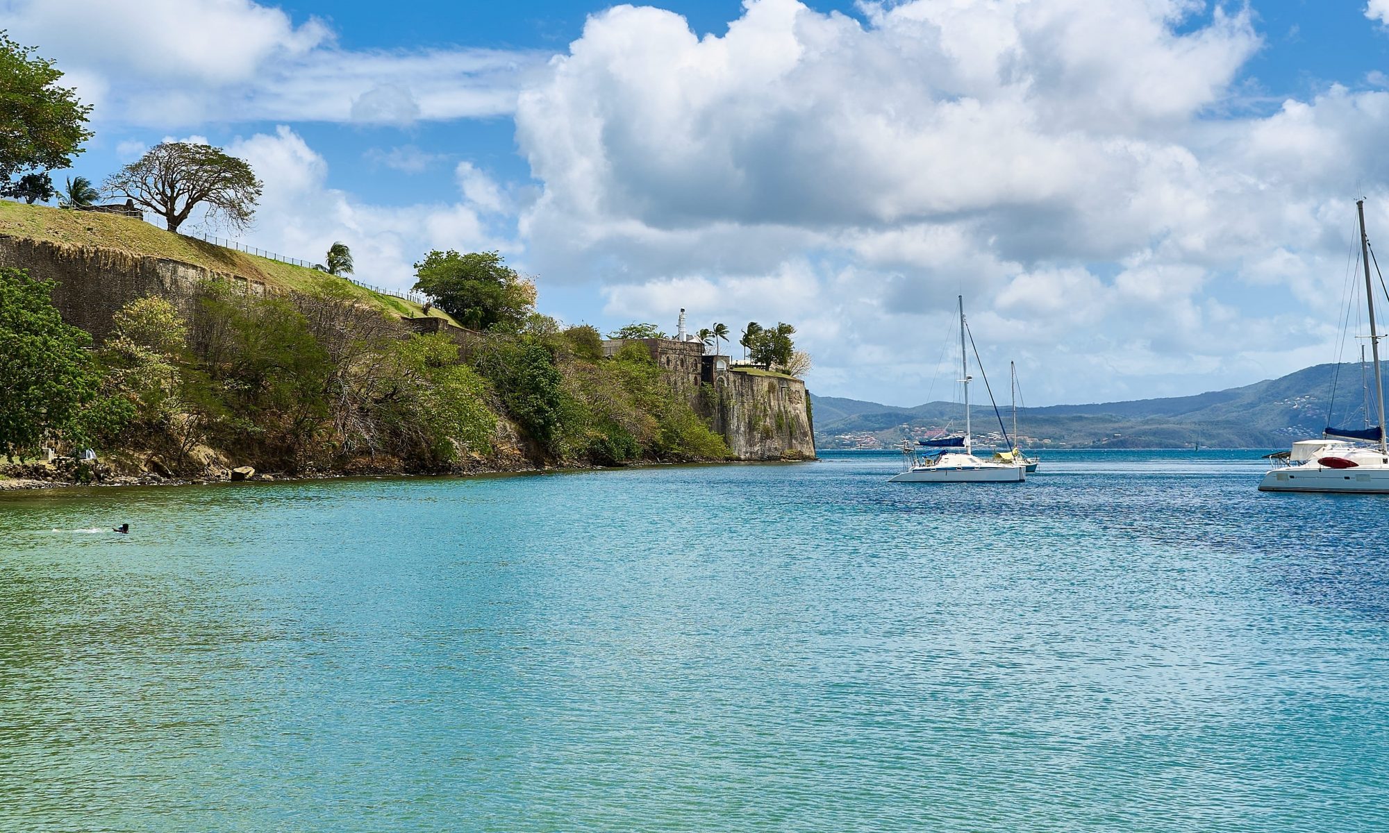 Calm beach with boats floating in the water and colourful trees framing the sandy shore.