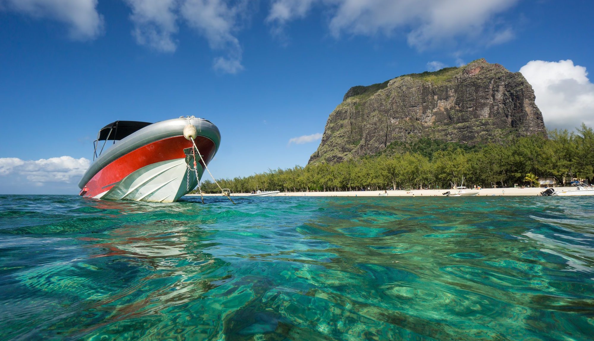 Un bateau flotte sur l'océan avec, en arrière-plan, une montagne majestueuse qui s'élève sous un ciel bleu limpide.
