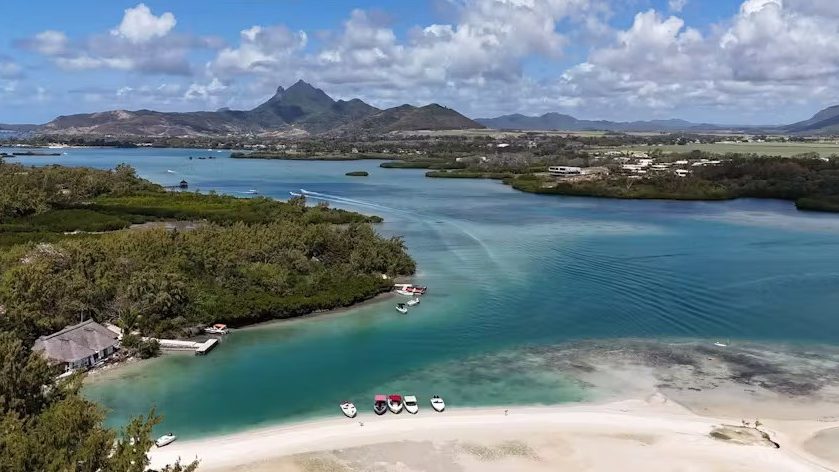 Vue aérienne d'une belle plage bordée de montagnes verdoyantes sous un ciel bleu clair.