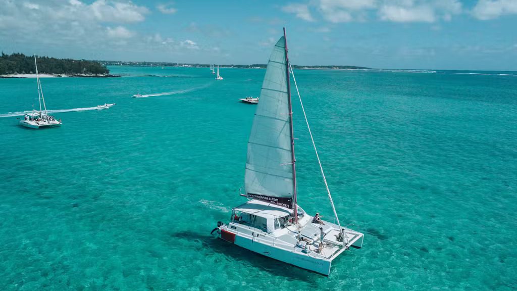 Un catamaran glisse sur les eaux claires et turquoises sous un ciel d'un bleu éclatant.