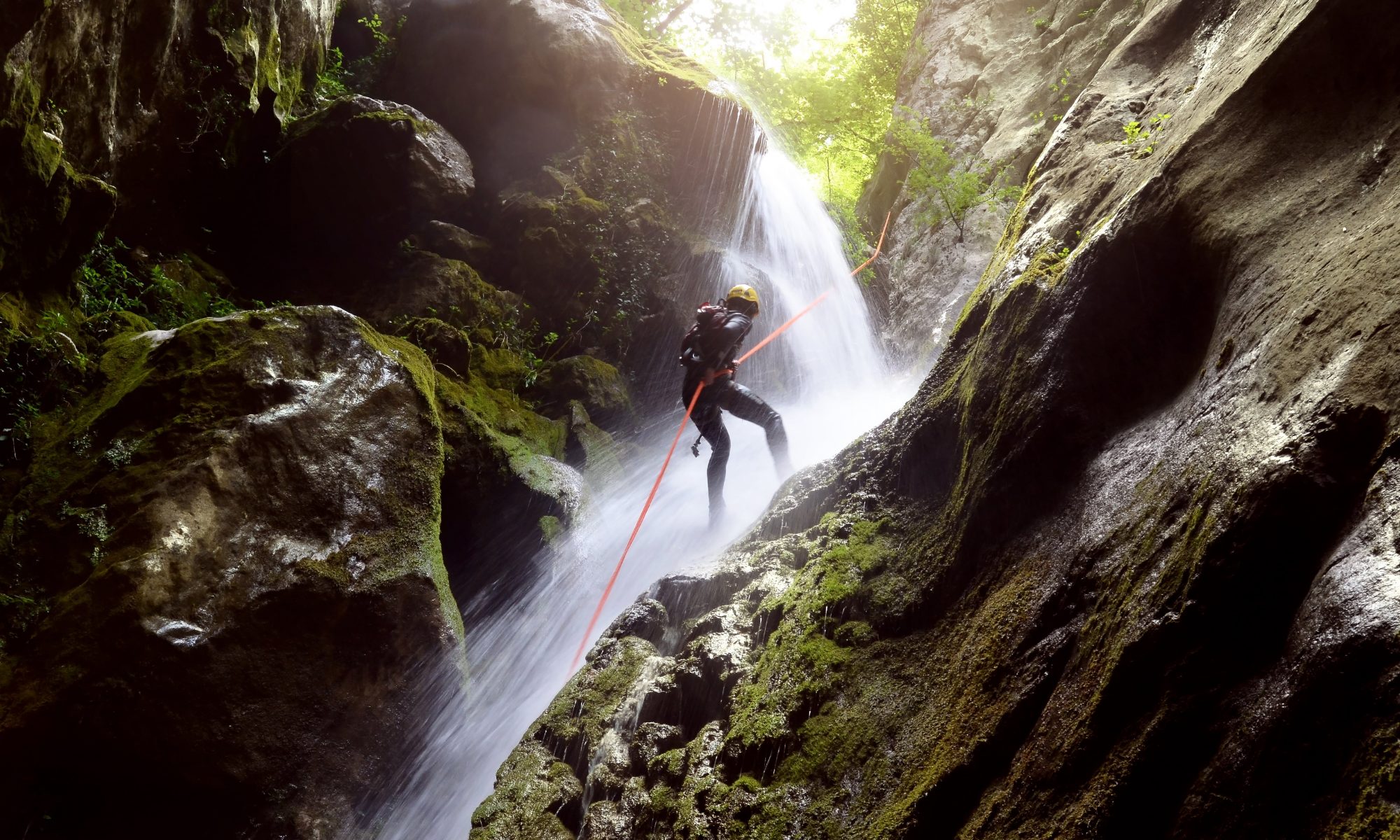A man rappelling down a waterfall in a gorge during canyoning.