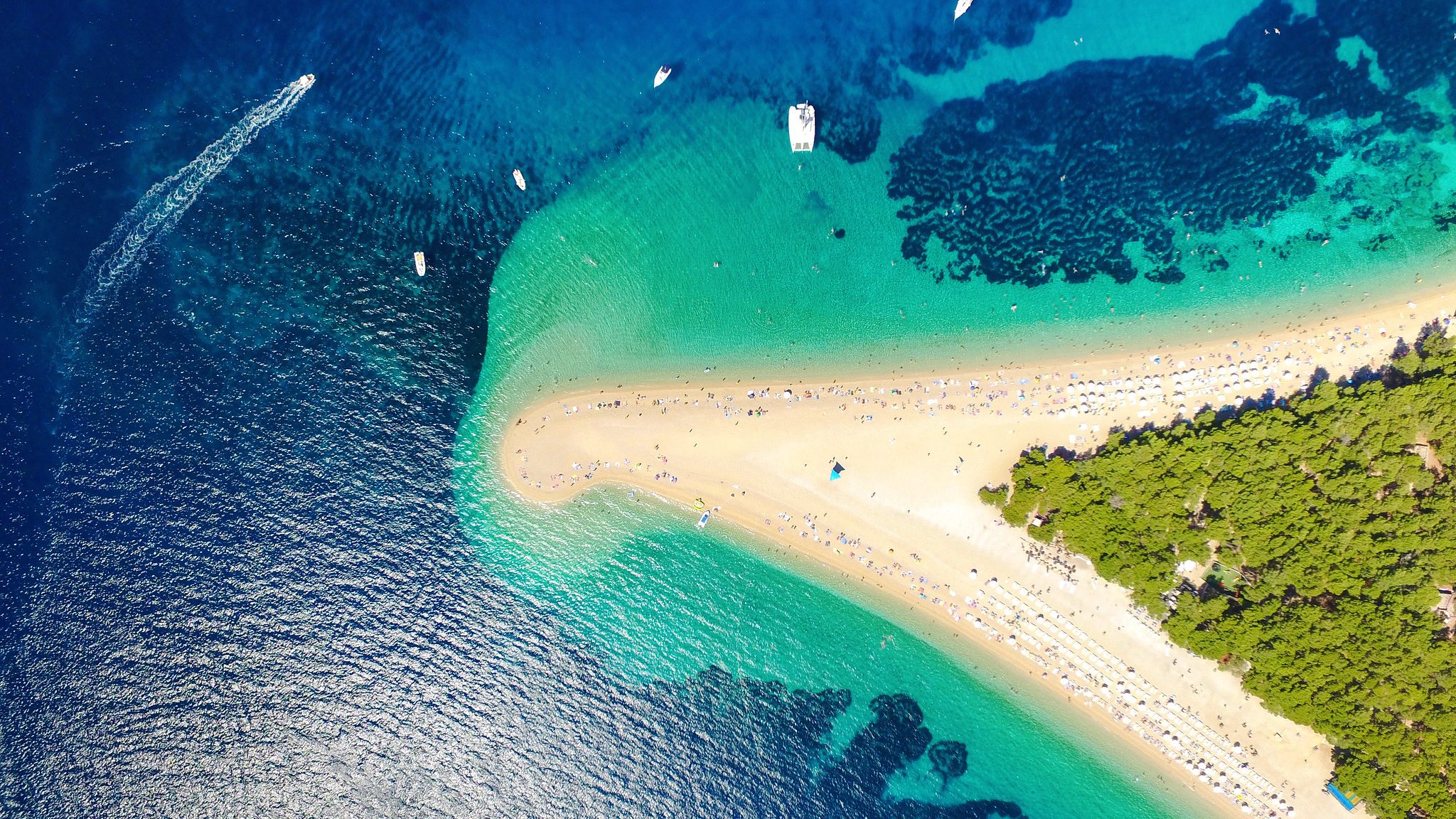 Aerial view of a sandy beach with turquoise waters surrounding a small, lush island in the distance.