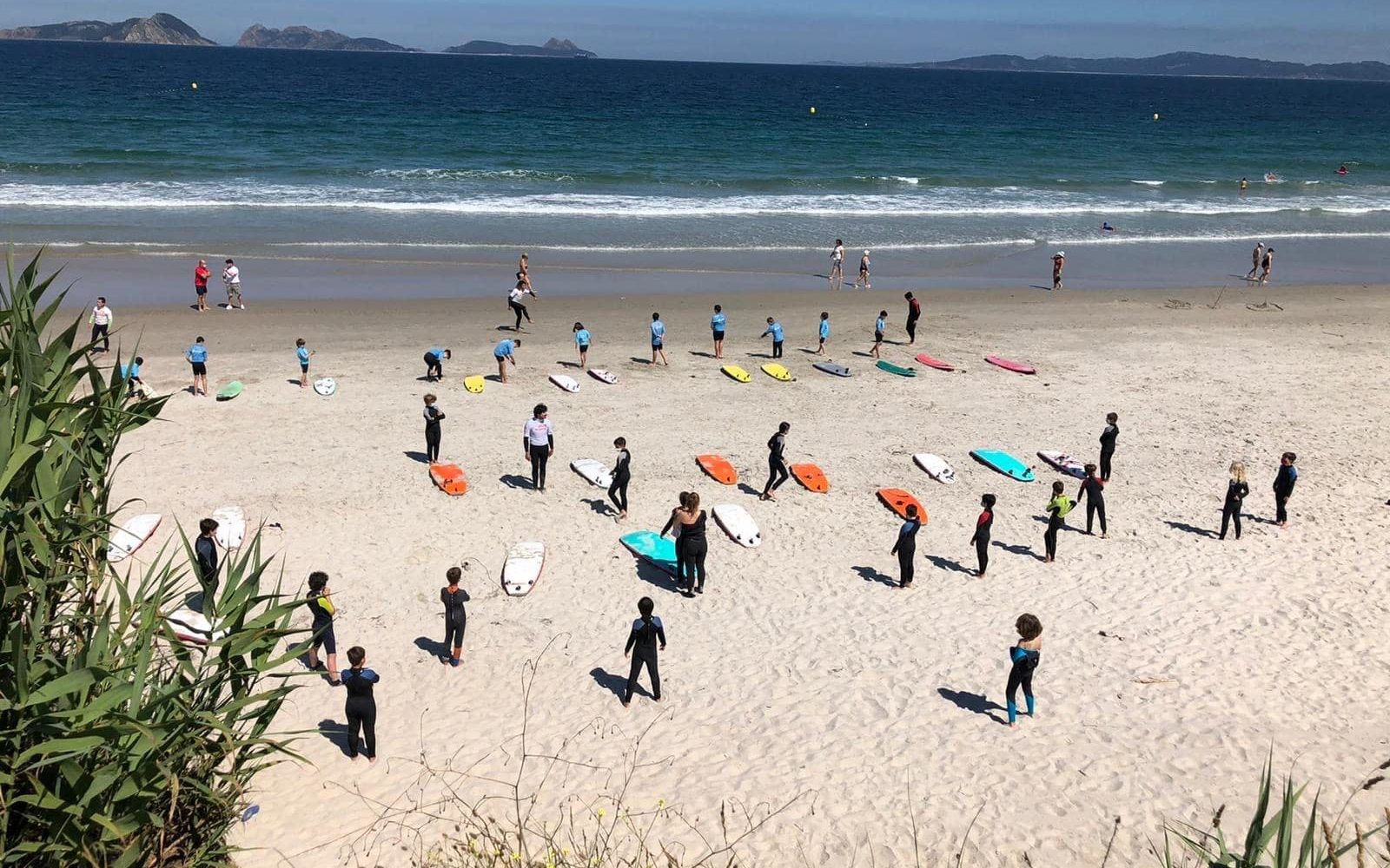 Mehrere Gruppen von Surfanfängerinnen nehmen an einem Surfkurs am Strand Praya La Lanzada teil.