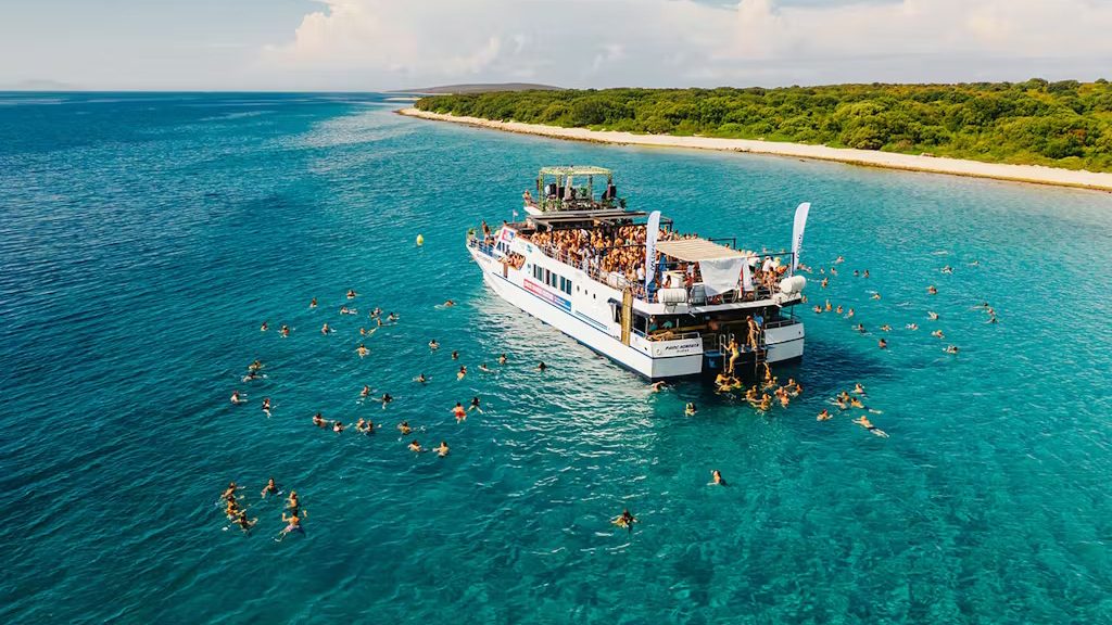 A boat floats in the ocean as people swim nearby, enjoying a sunny day on the water.