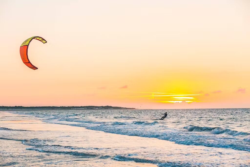 A kite surfer surfing on Velika Plaža with the sun setting in the background, making the sky orange.